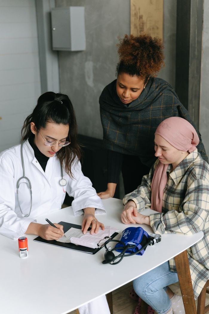 A female doctor consults two patients at a desk in a medical clinic, emphasizing diversity and professionalism.